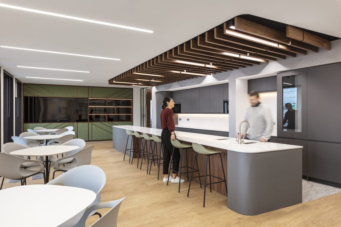 A man and a woman are shown chatting over the bench inside the staff breakout area at Amundi offices.