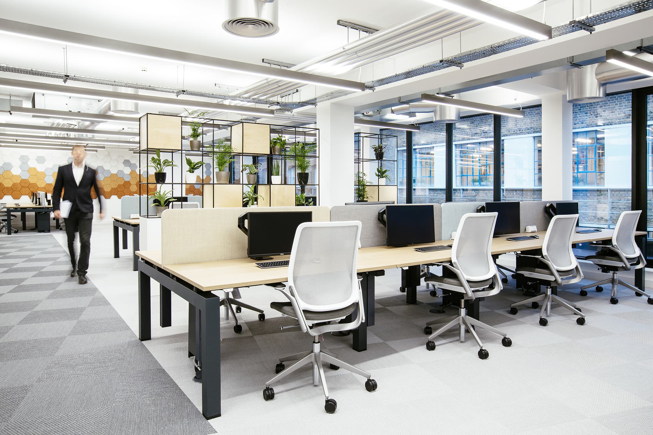 AIS inclusive workplace design and build for Versus Arthritis open plan work zone with banks of desks and a person walking down the hallway