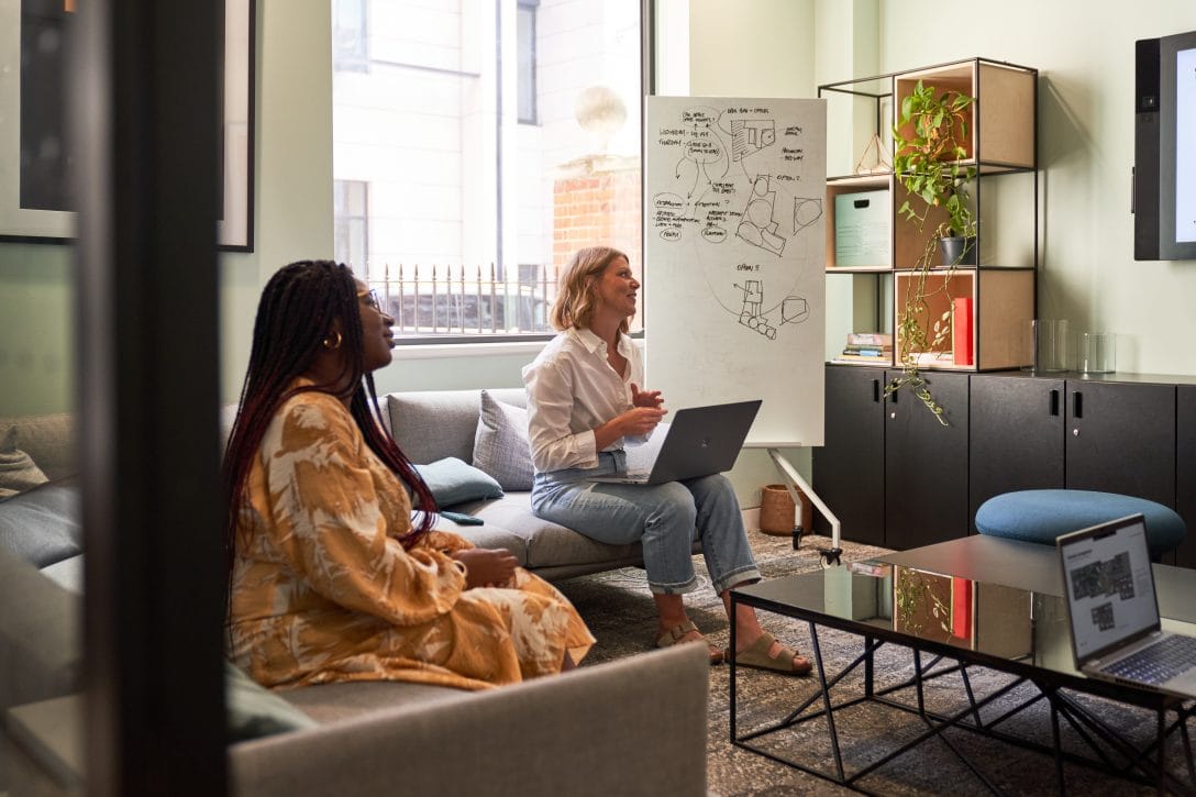 Two woman are shown in an office meeting room working together.