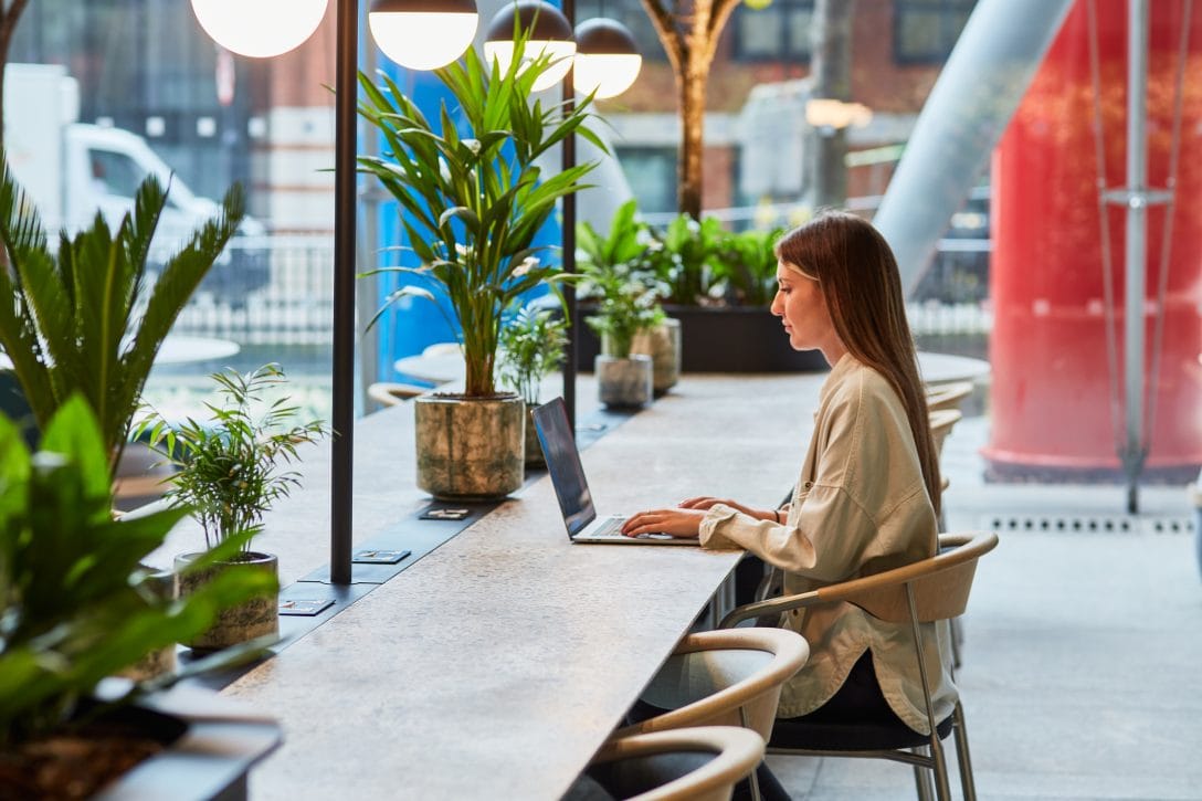 A girl is shown working at a biophilia office desk which features in-built planters. 