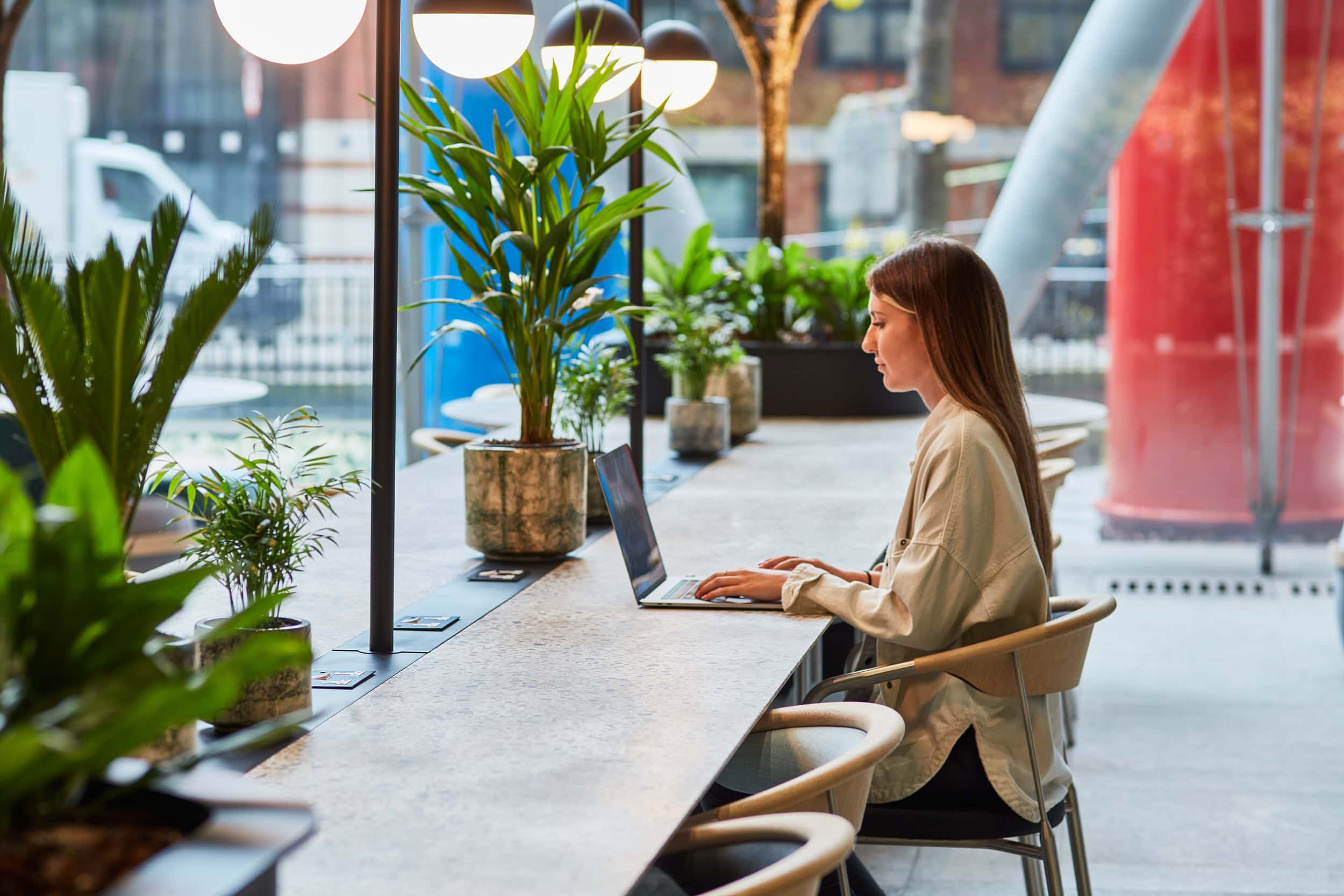 A girl is shown working at a biophilia office desk which features in-built planters.