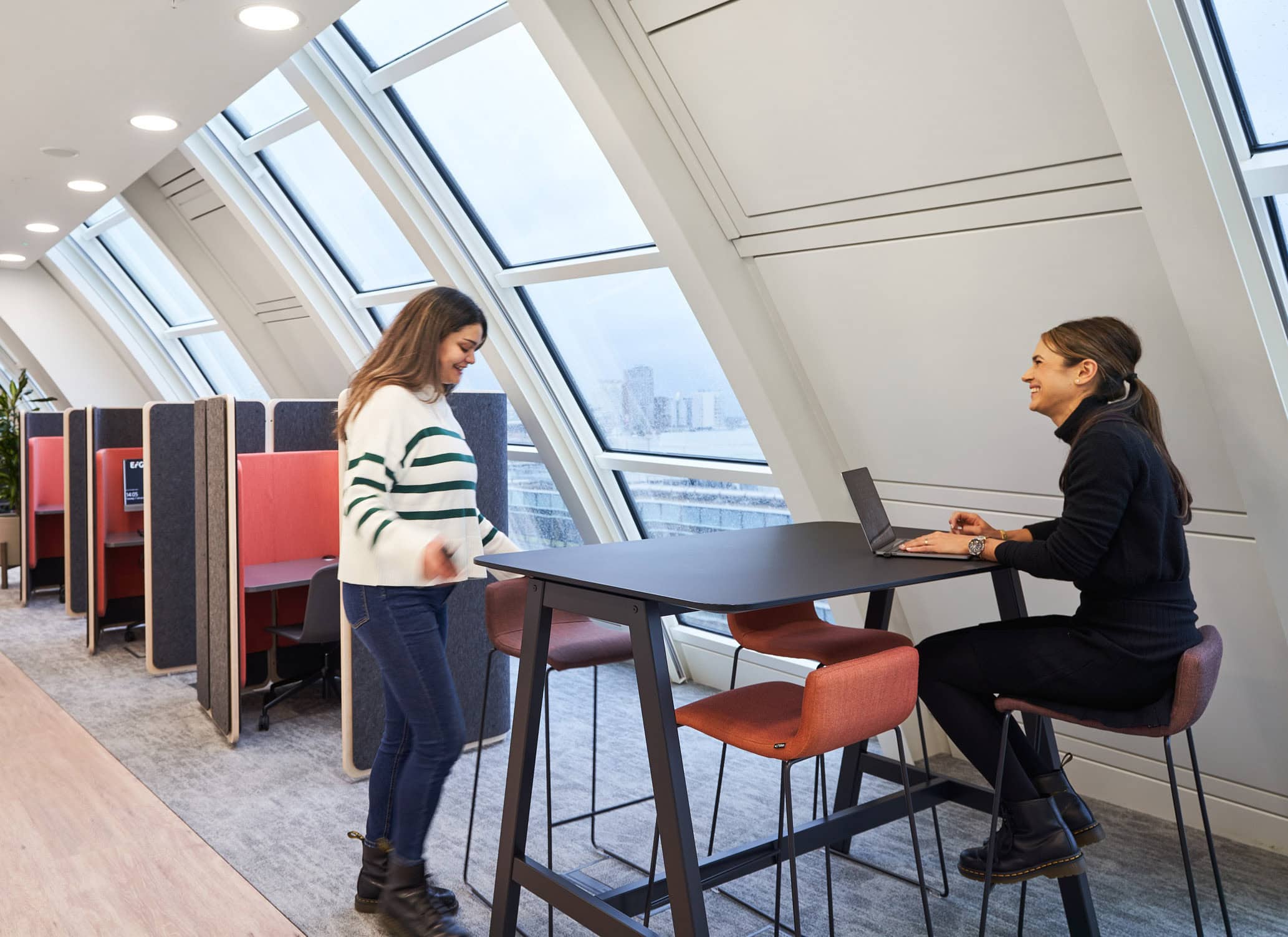 Two women are collaborating at a workstation within an office crafted to prioritise optimal workplace mental health.