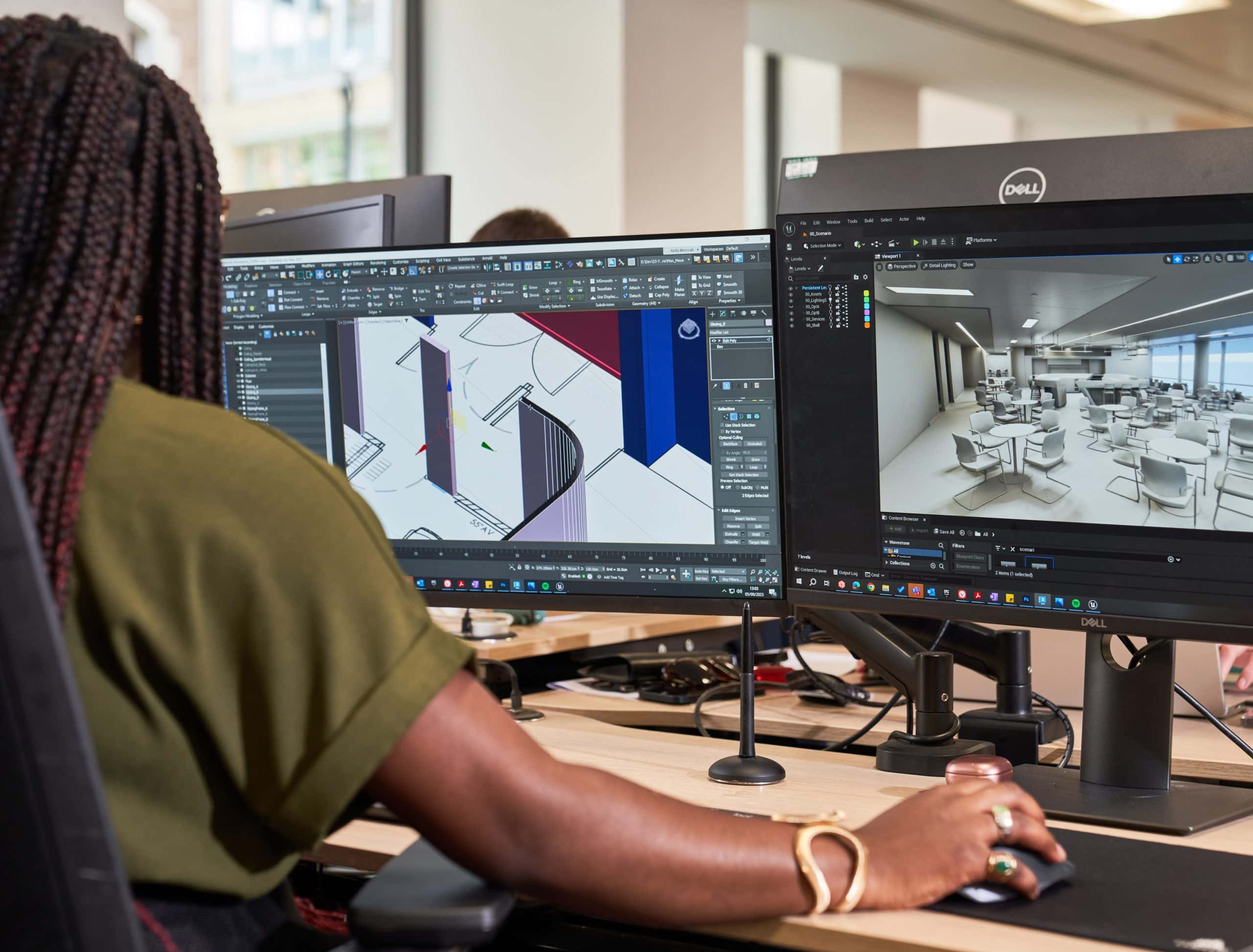 Woman sits at computer working on an AIS 3D office model. Her screen shows the 3D model in wireframe stage.