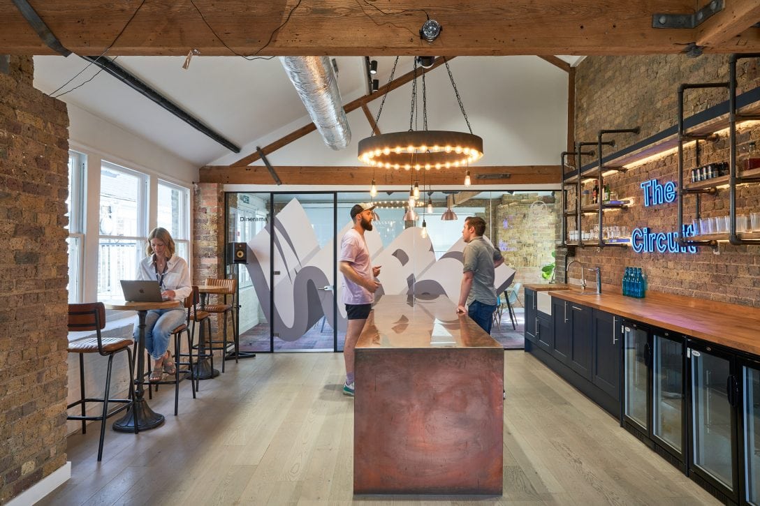Casually dressed young employees are shown in an office tea point chatting over a coffee.