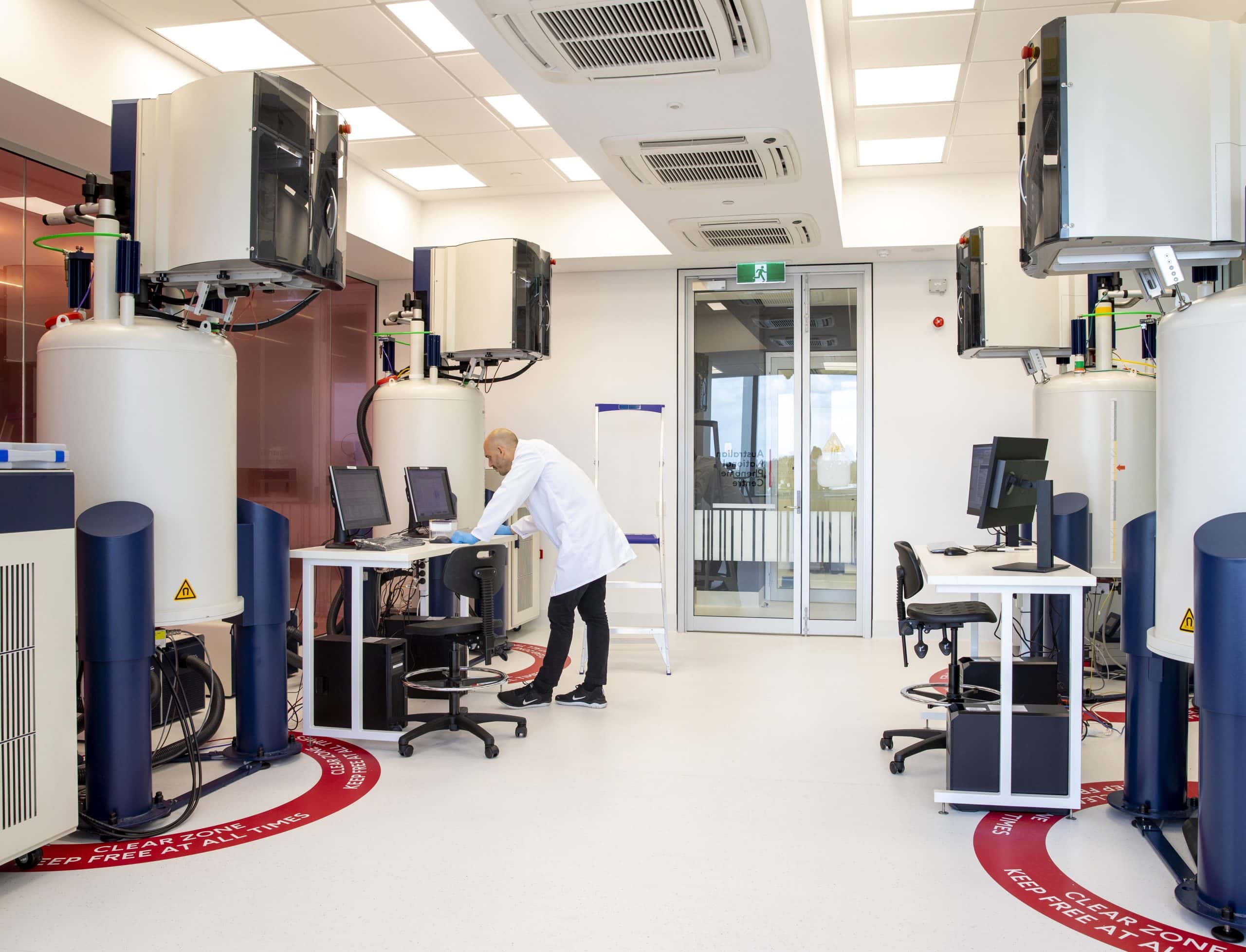 A male scientist stands in a laboratory design by AIS. There is a lot of large equipment surrounding him.