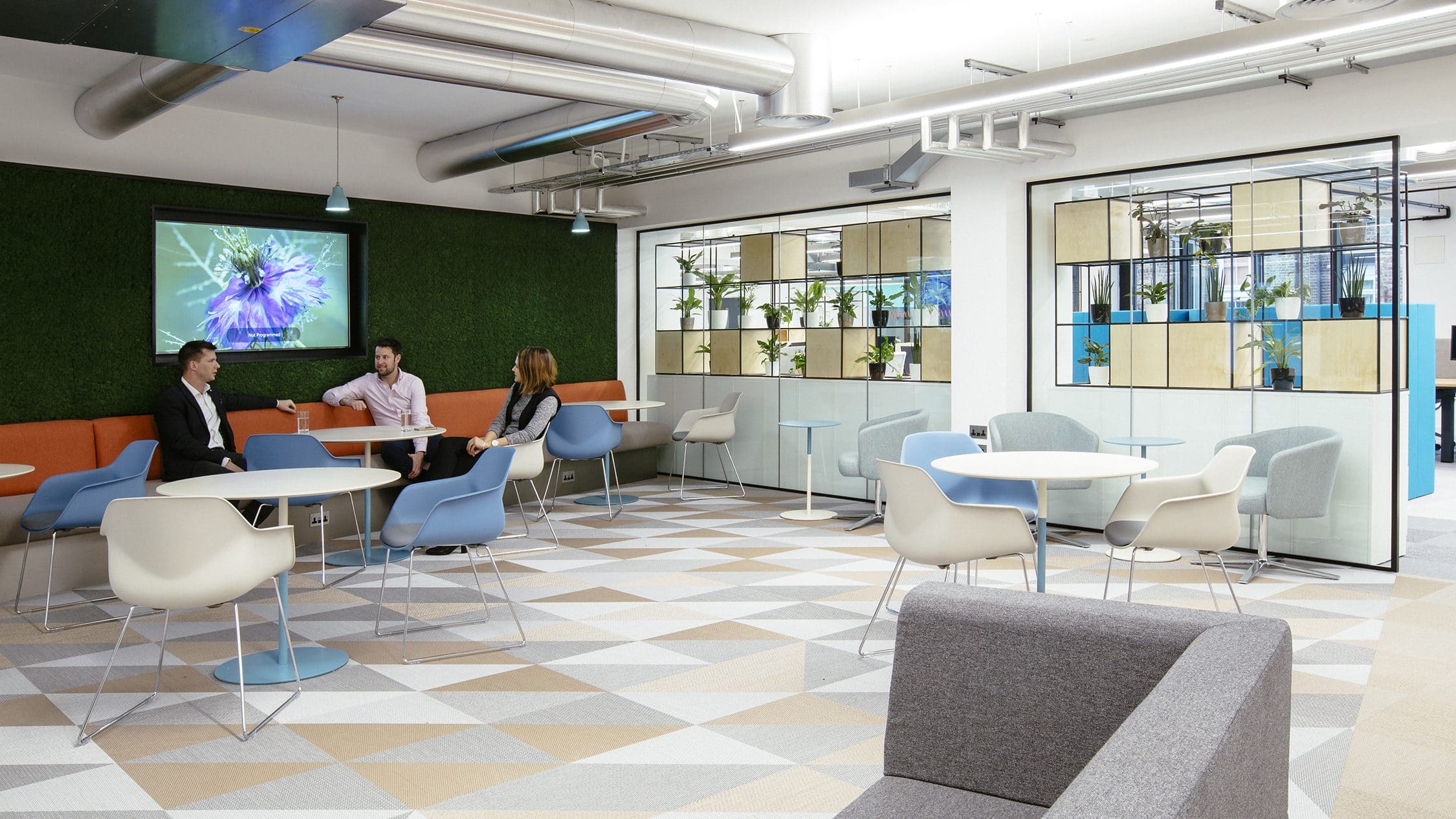 Employees are shown sitting in an office breakout area in front of a green wall helping to contribute to workplace ESG.