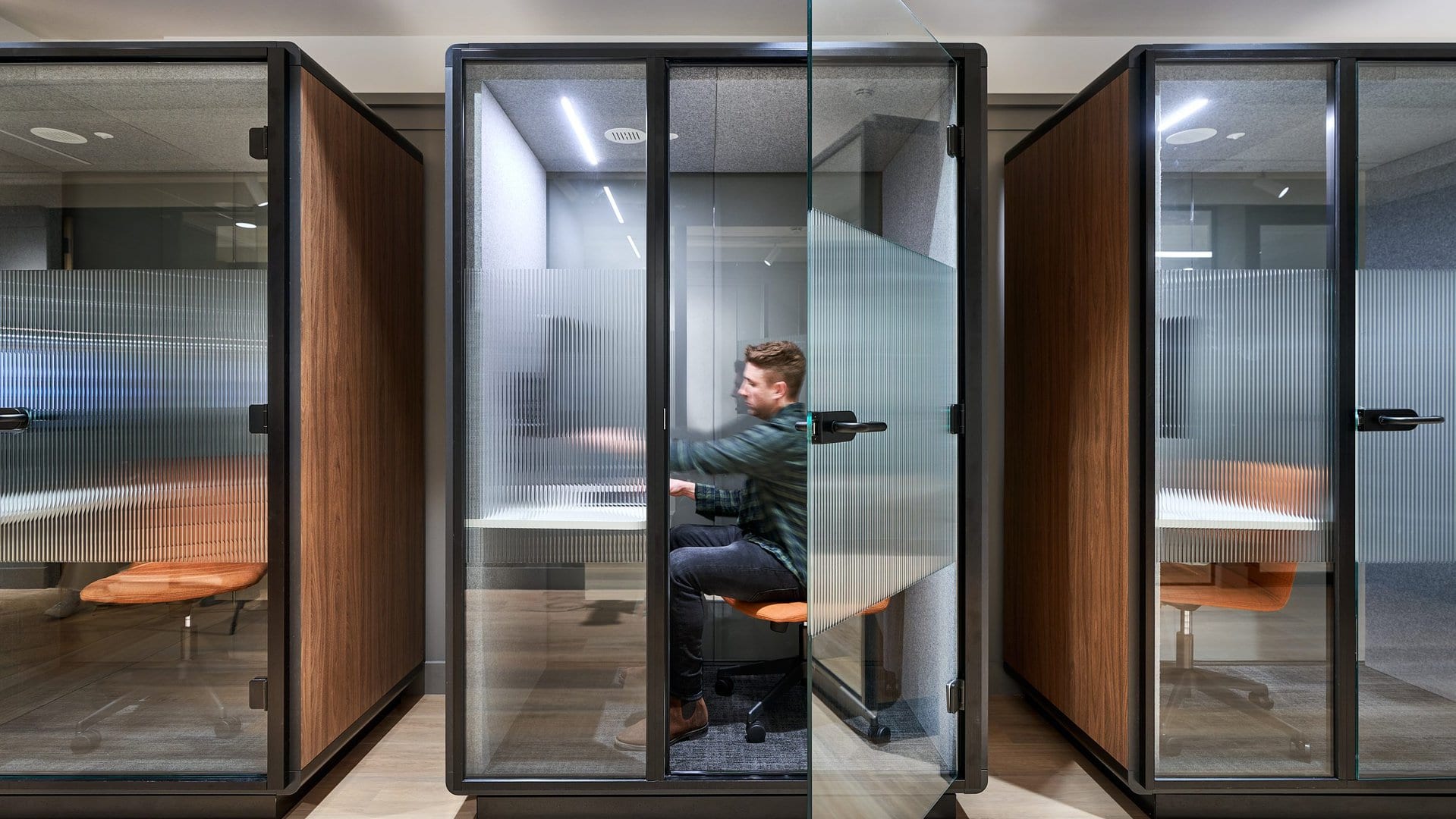 A man sits working in a privacy booth inside an office.