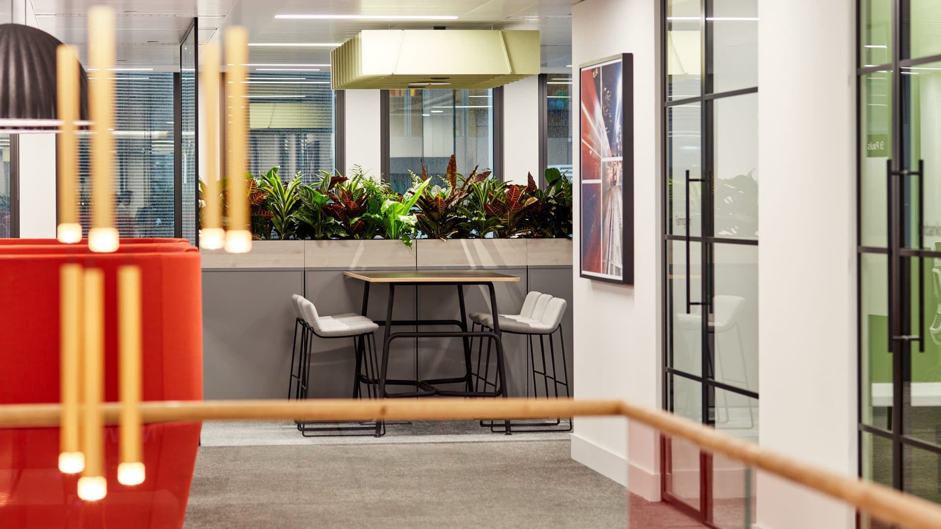 A feature pendant light is shown in the foreground of an image of an office. Some meeting room doors are to the right and a high bench top table is at the back of the room.