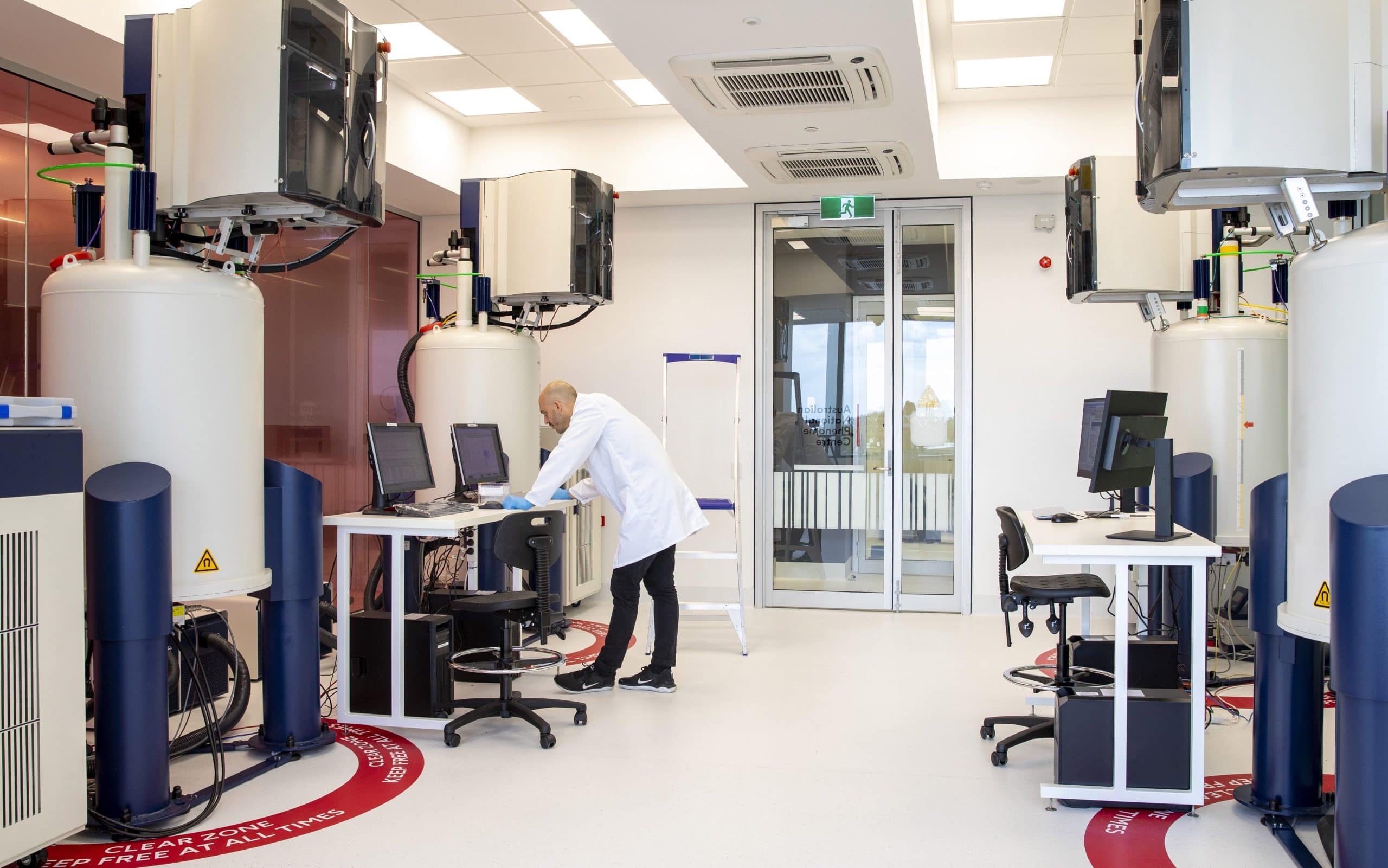 A male scientist stands in a laboratory design by AIS. There is a lot of large equipment surrounding him.