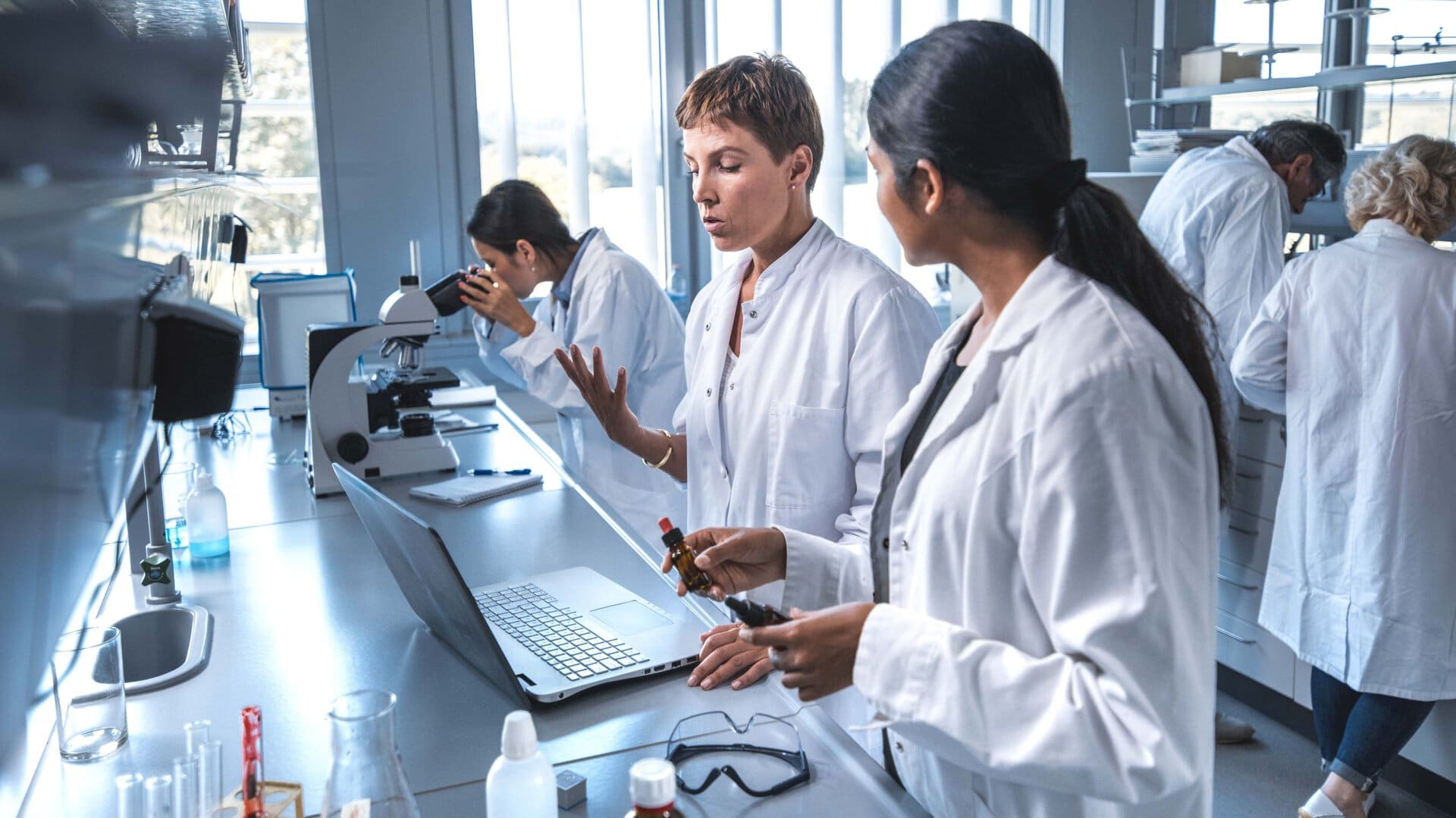 Researcher discussing with colleague over laptop in a laboratory.