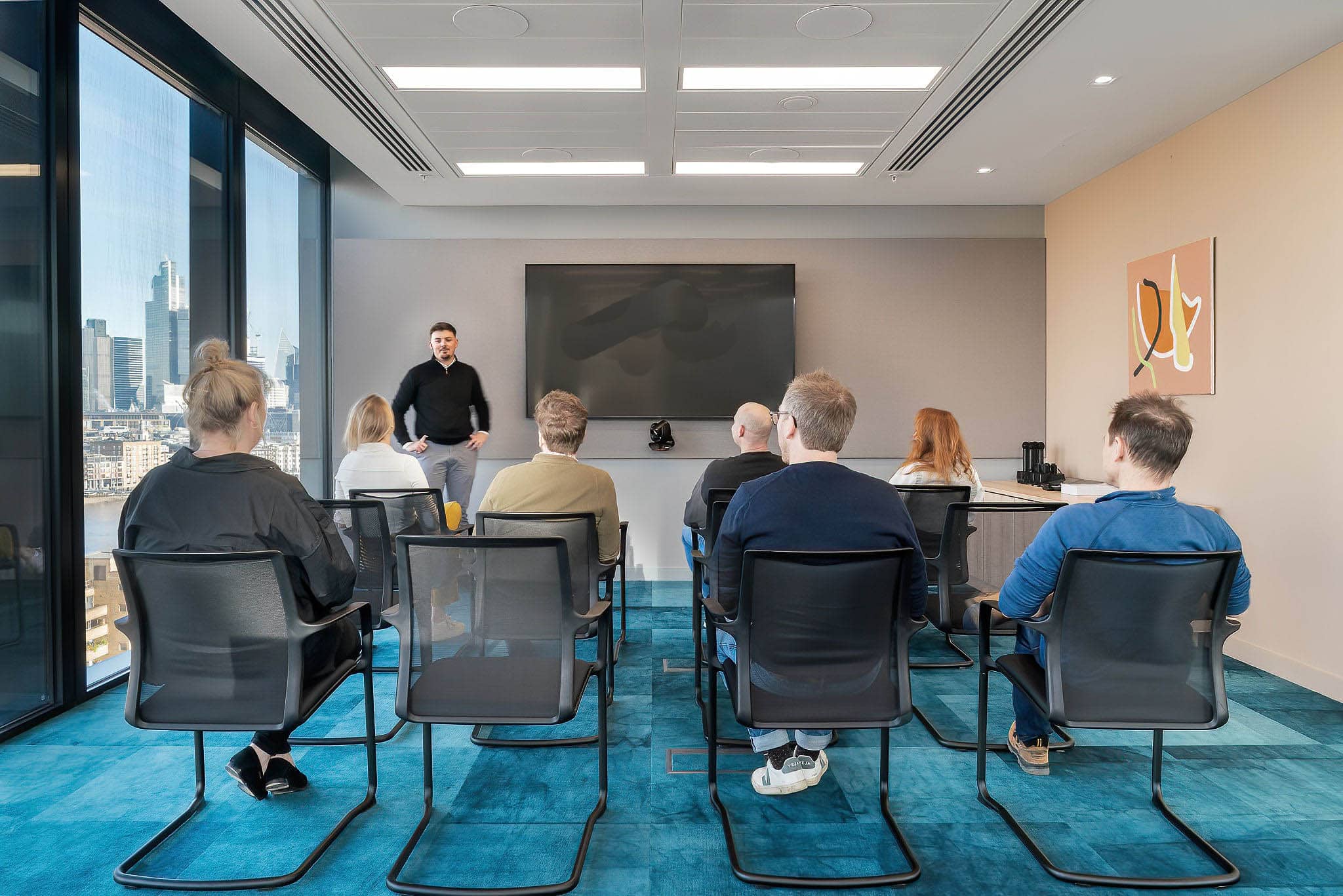 Employees are shown seated in rows of chairs in a training meeting taking place in an office meeting room.