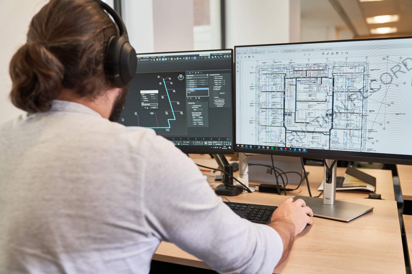 Man at 2 computer screens creating a detailed 3D drawing using technical software